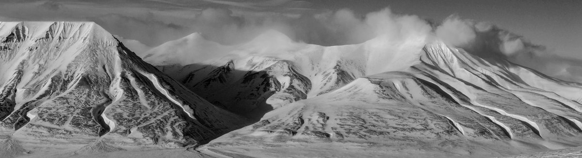 UAV operator flying a quadcopter over snow-covered terrain in Svalbard, survey stakes visible below