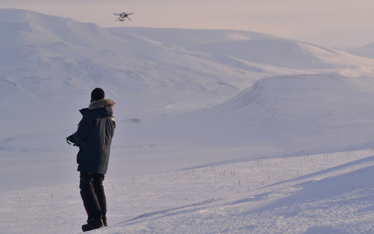 Operator flying the white quadcopter over the GCP network at a Longyearbyen survey site, April 2015. The stakes mark the ground control points used to georeference the point cloud.